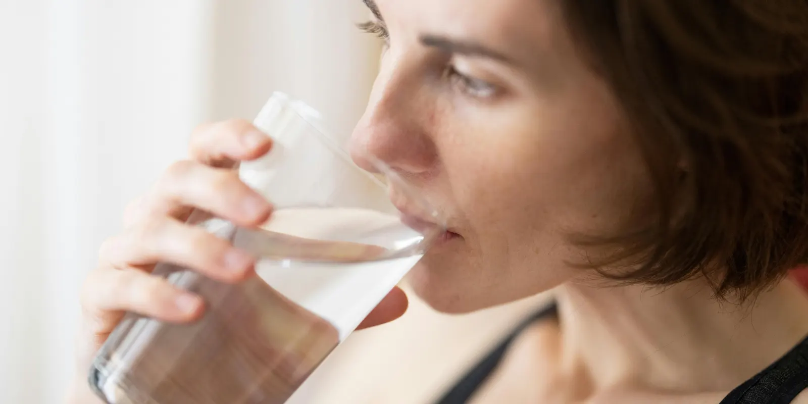 Frau genießt ein Glas Wasser, behandelt mit einem Wasserenthärter, der Kalkablagerungen verhindert, ohne natürliche Mineralien zu entfernen